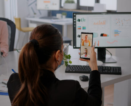 Executive business woman wearing protective face mask using phone for online videocall conference